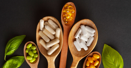 Cuillères en bois contenant différents compléments alimentaires en gélules, capsules et comprimés, présentés sur fond noir avec des feuilles vertes – MyNutriForm